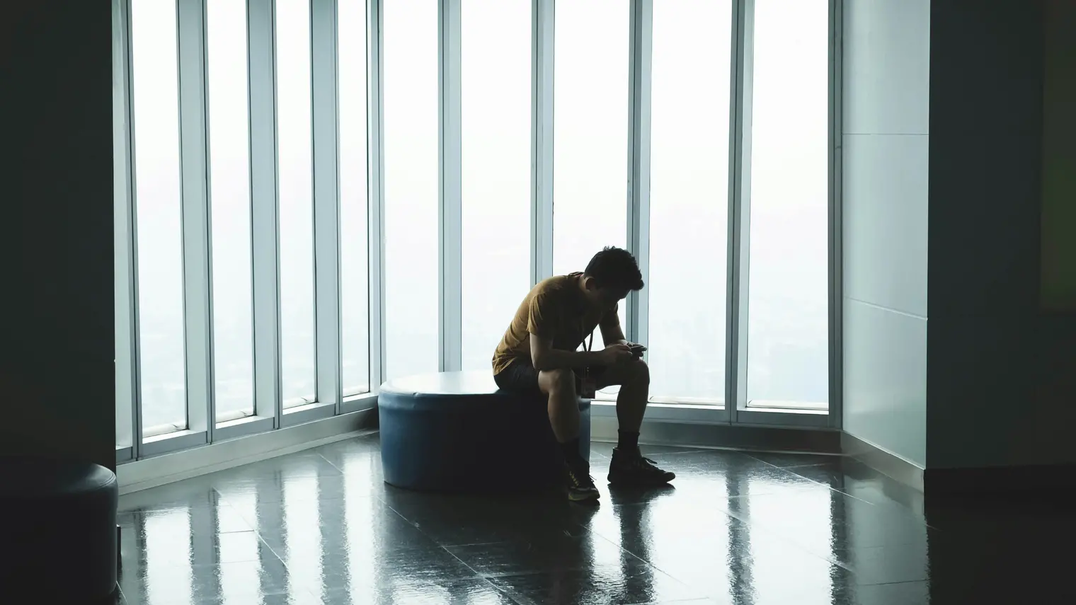 a lonely man sitting in a chair with large windows beside him