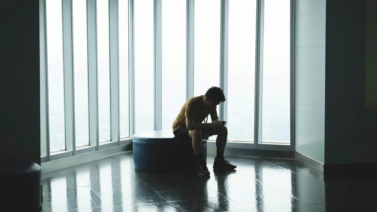 a lonely man sitting in a chair with large windows beside him