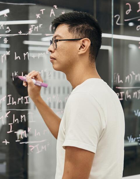 A man writing algorithms on a glass wall.