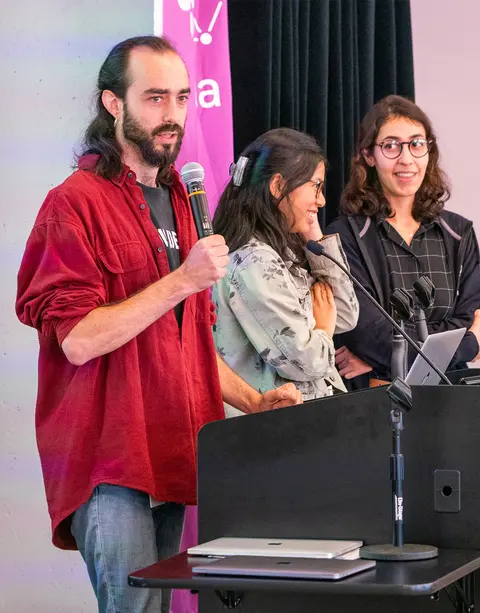 A man and two women speaking on stage at a town hall. 