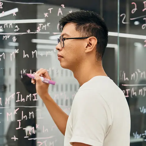 Un homme écrit des algorithmes sur une paroi en verre.