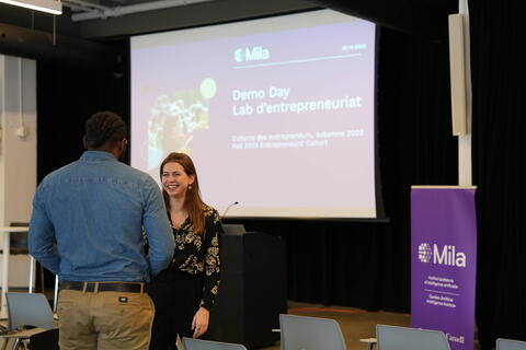 Two participants of Mila's Demo Day talking together in front of the stage