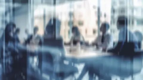 Blurred, abstract image of people sitting around a conference table.
