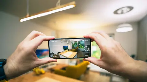 Hands holding a smartphone to photograph the interior of a brightly lit room.