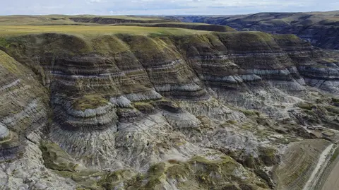 Landscape view of layered rock formations and grassy hills.