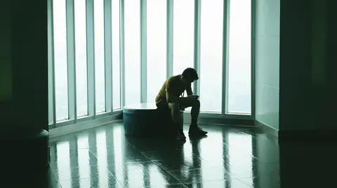 A figure sitting alone near a large, bright window. 