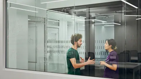 A young man and a young woman are talking in a hallway. 