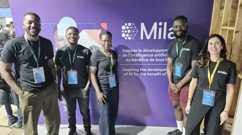 A group of people posing in front of Mila's booth at Indaba 2025.