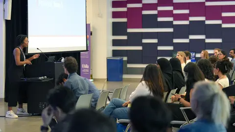 A woman giving a lecture in front of an audience. 