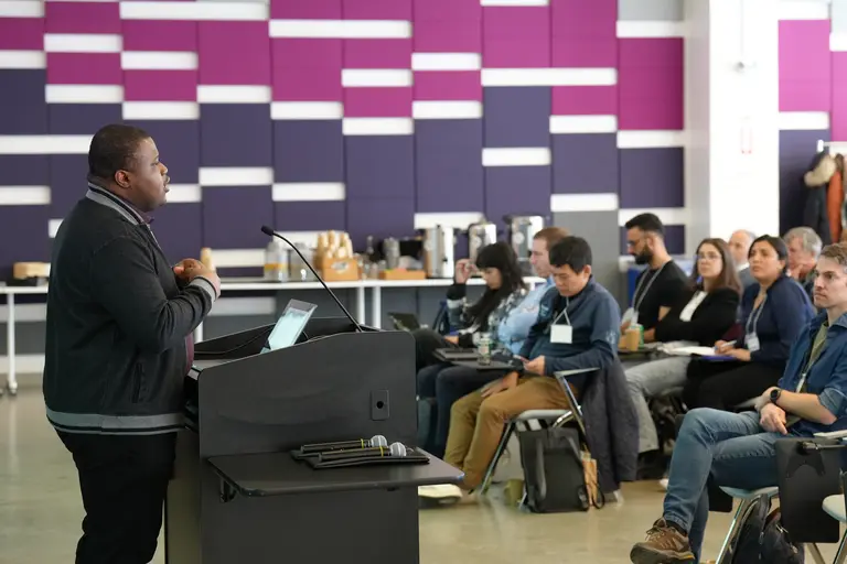 Picture of David Adelani speaking in front of an audience at Mila