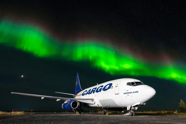 Photo d'un avion au sol pendant la nuit avec une aurore boréale verte en arrière-plan.