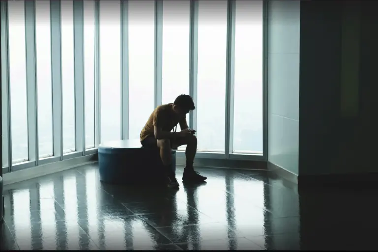 A young man, alone on a bench looking at his pone