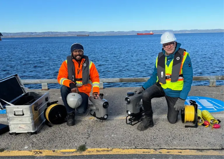 Photo de Jorawar Singh Dham, étudiant à Mila, et Laurent Ferrier posant sur un quai avec leur équipement pour scanner des structures sous-marines.