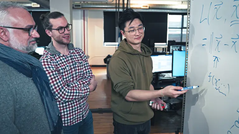 Members of the Ubisoft-Mila Chair team discuss algorithms together in front of a whiteboard.