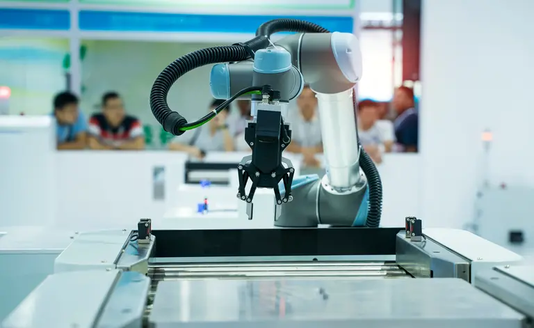People watching a robotic arm at work in a factory.