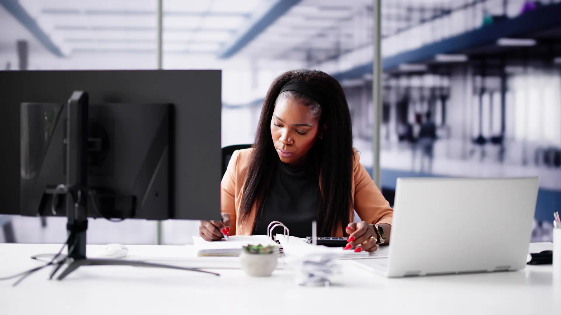 a young black women working at her desk with a screen and a laptop in front of her