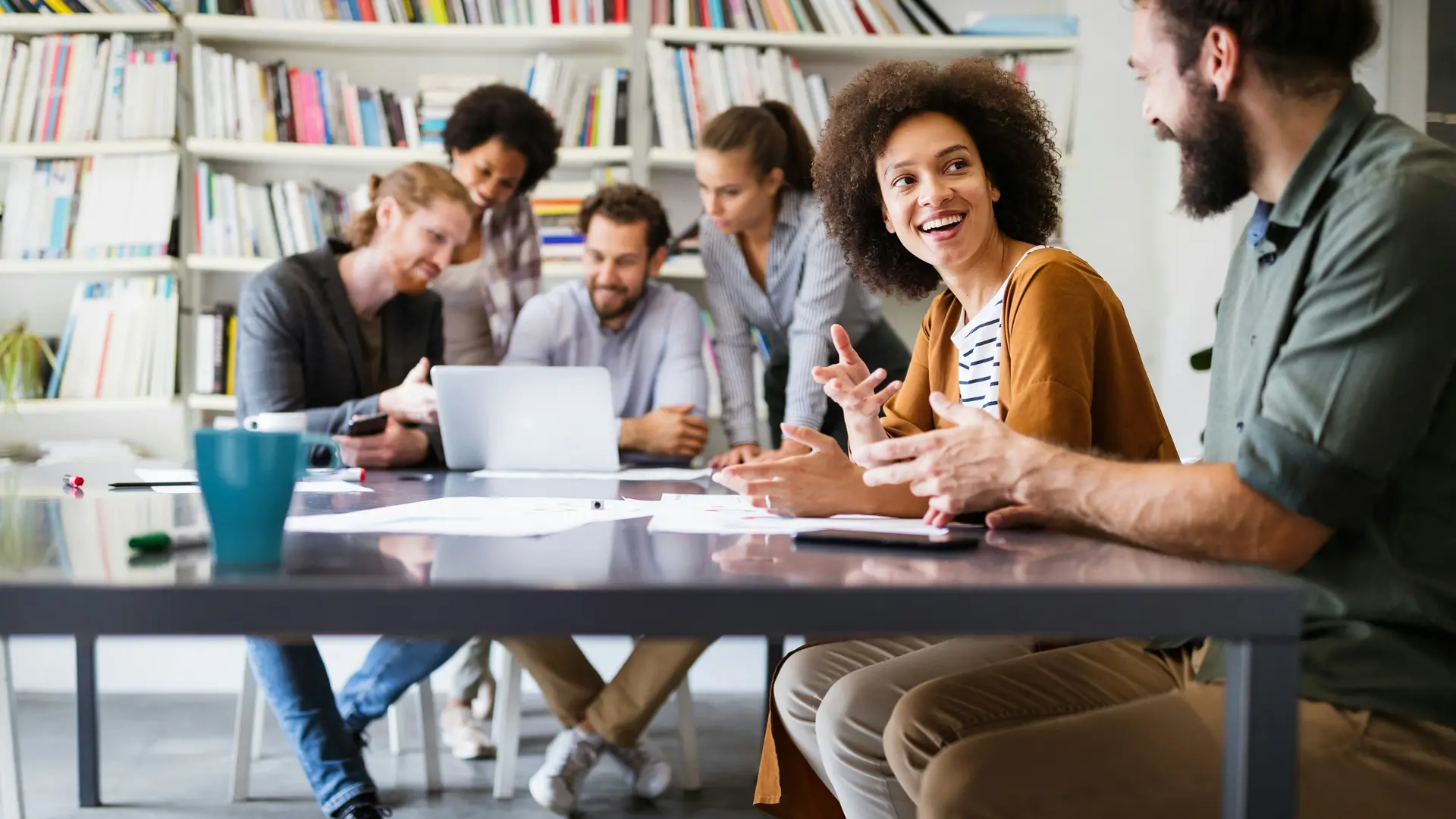 Picture of 6 people sitting at a table on a library and discussing over a computer
