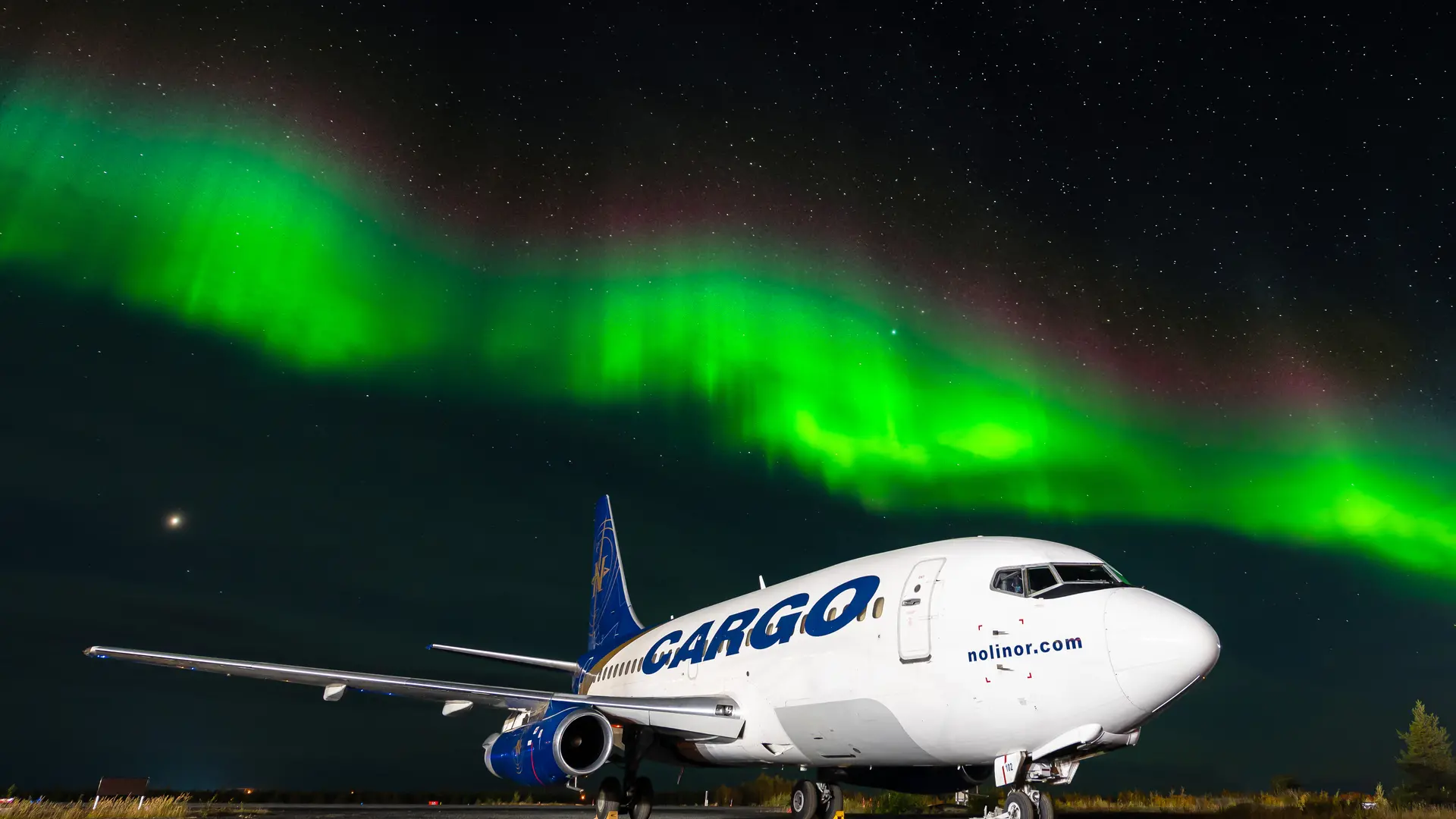 A picture of a plane on the ground during night time with green northern lights in the background