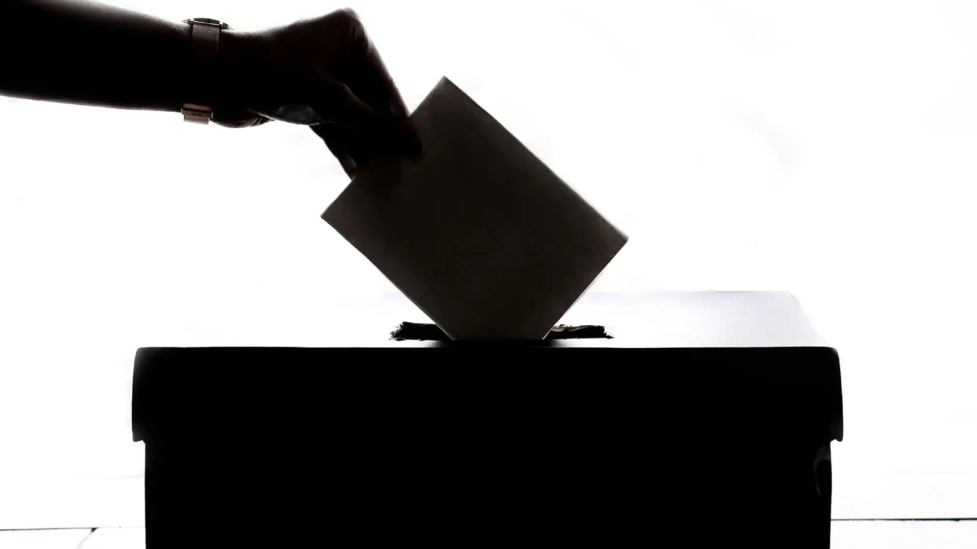 Photo en noir et blanc d'une main qui dépose un bulletin de vote dans la boite électorale
