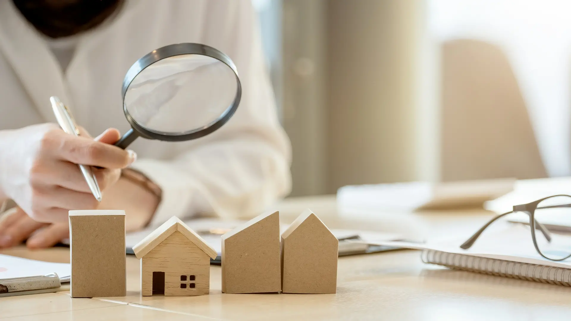 photo d'une personne avec une loupe qui regarde des maquettes de maison