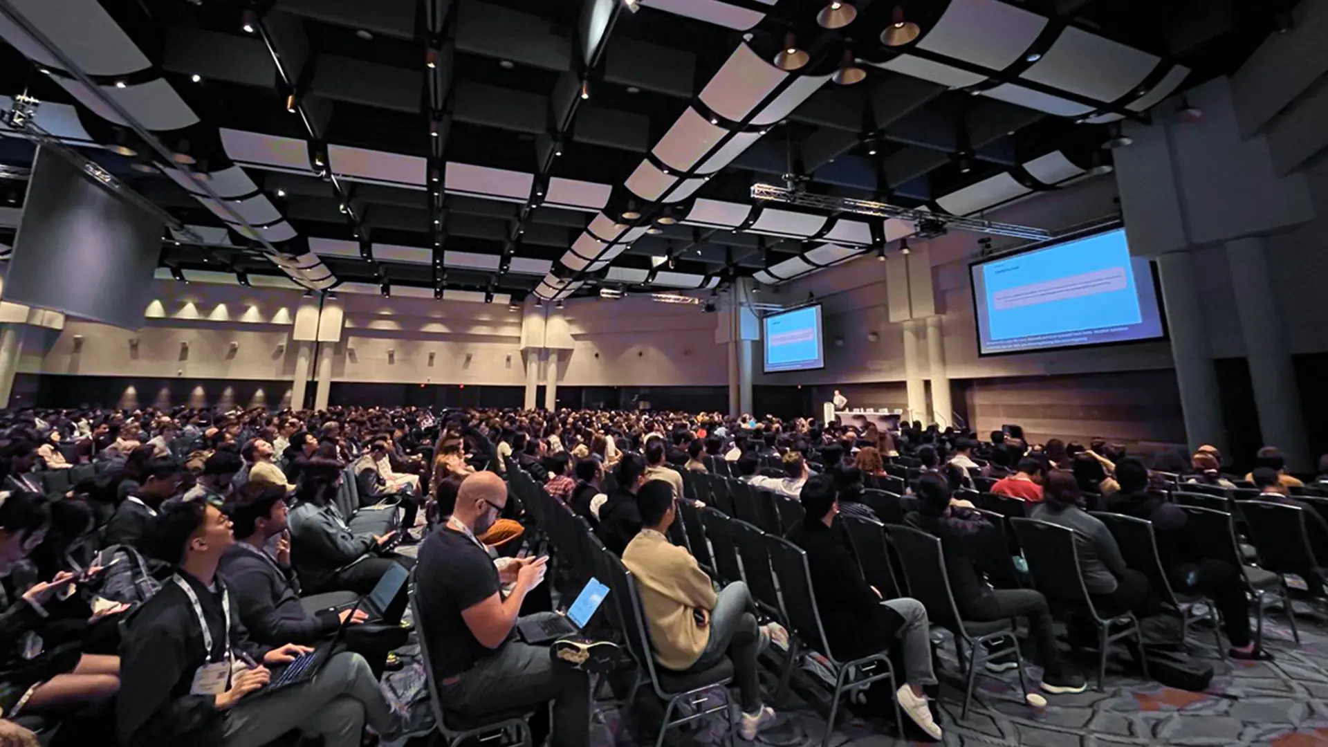 A crowd of people listening to a presentation at a conference.