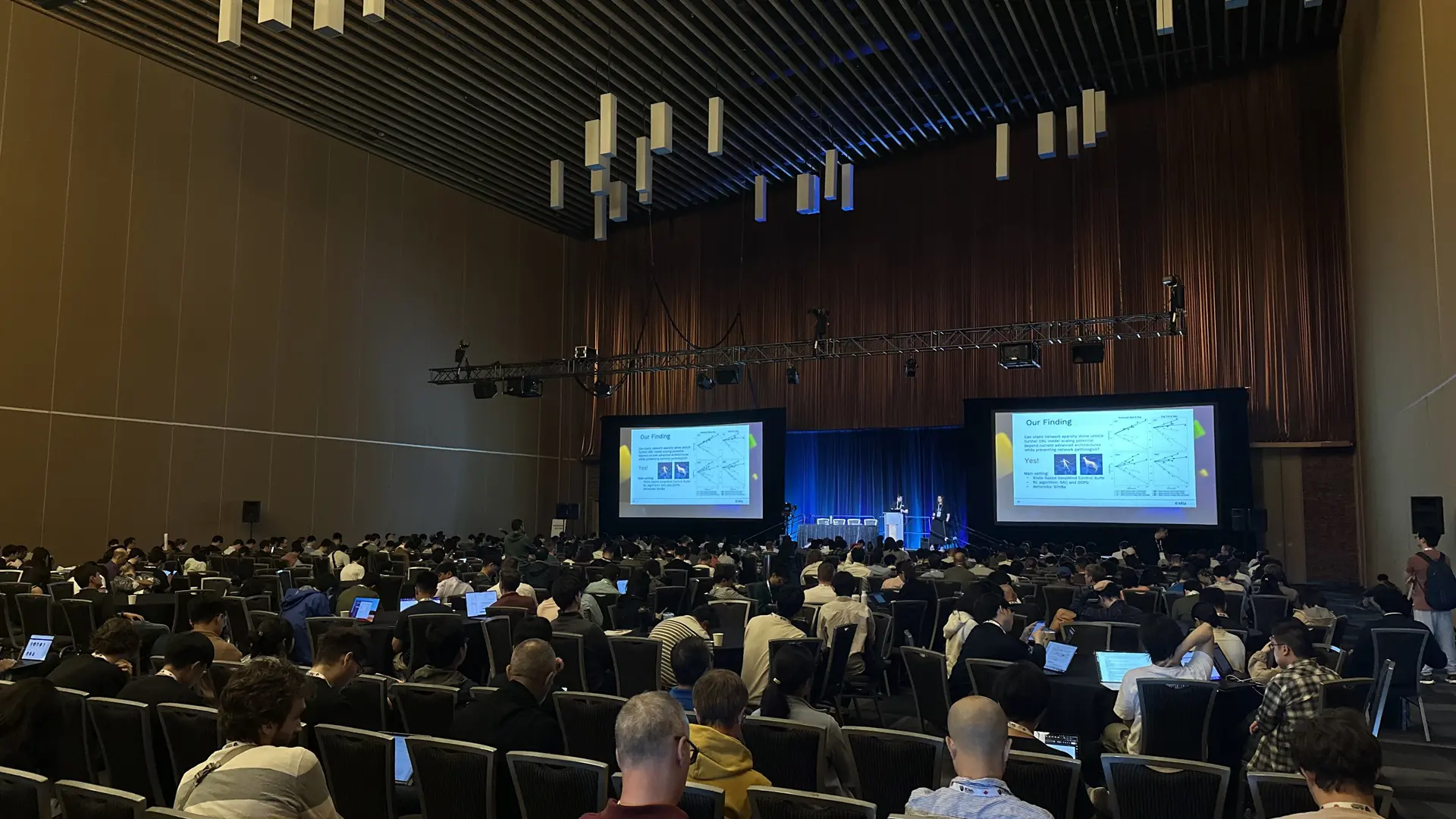 a picture of 2 mila researchers presenting their research paper in oral presentations on stage in front of a crowd at ICML