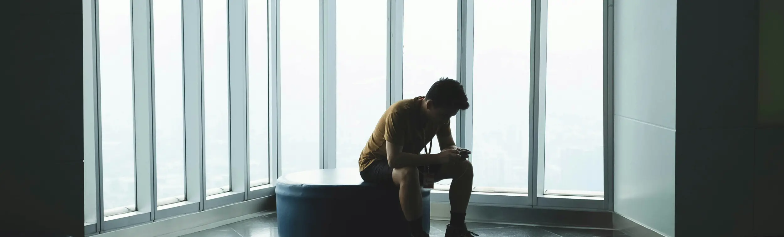 a lonely man sitting in a chair with large windows beside him