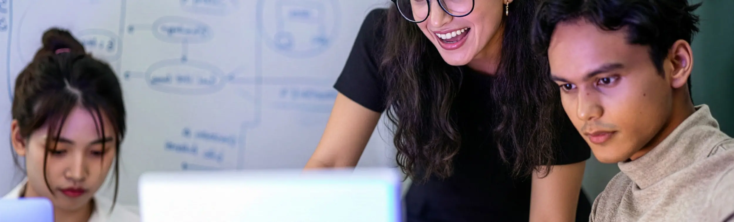 three people working in front of one computer with post it on a white table beside them