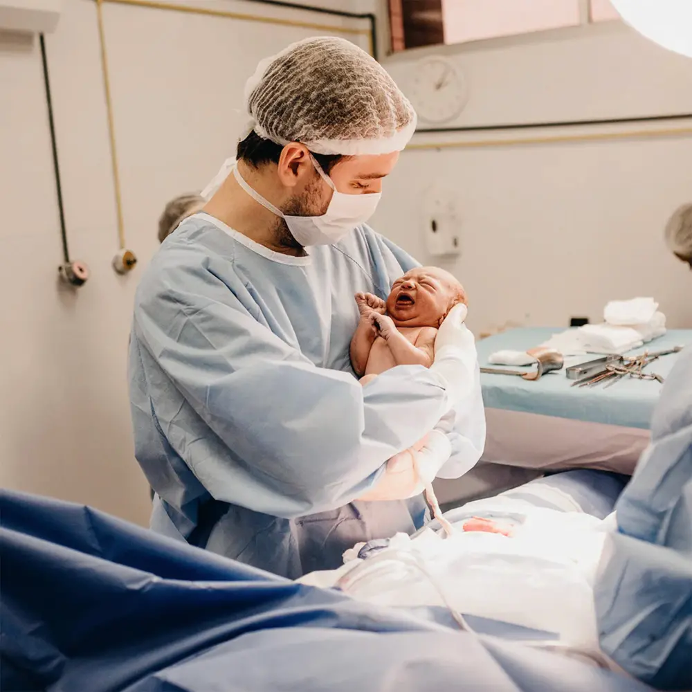 Man in lab suit and mask carrying a newborn baby in his arms. 