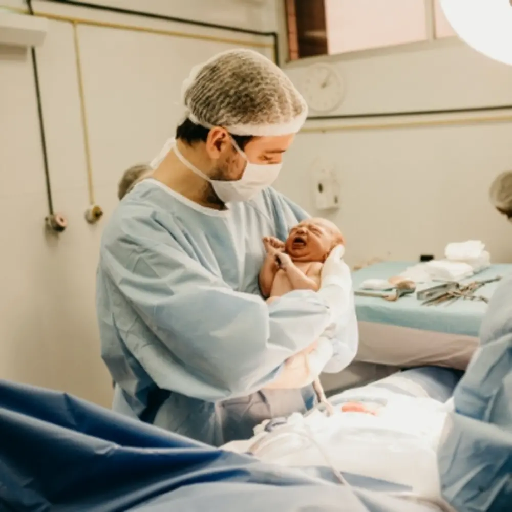 Homme en combinaison et masque de laboratoire portant un nouveau-né dans ses bras.