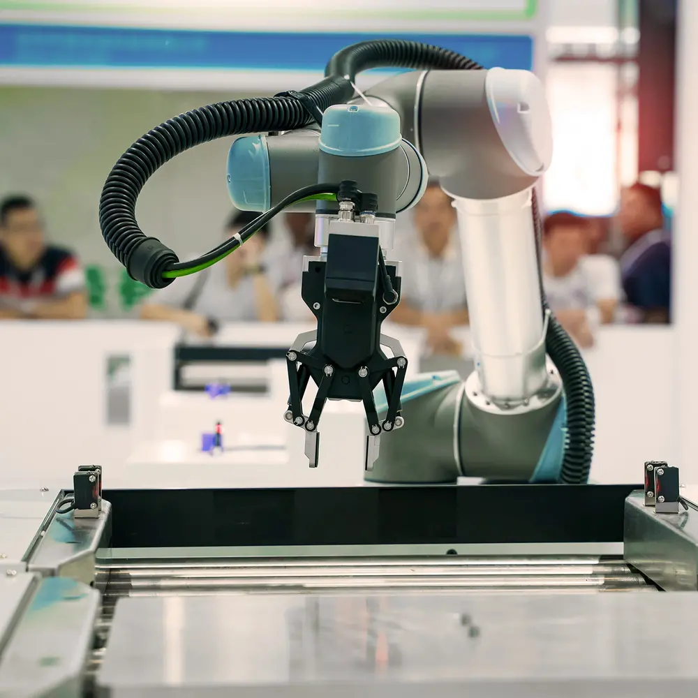 People watch a robotic arm at work in a factory.