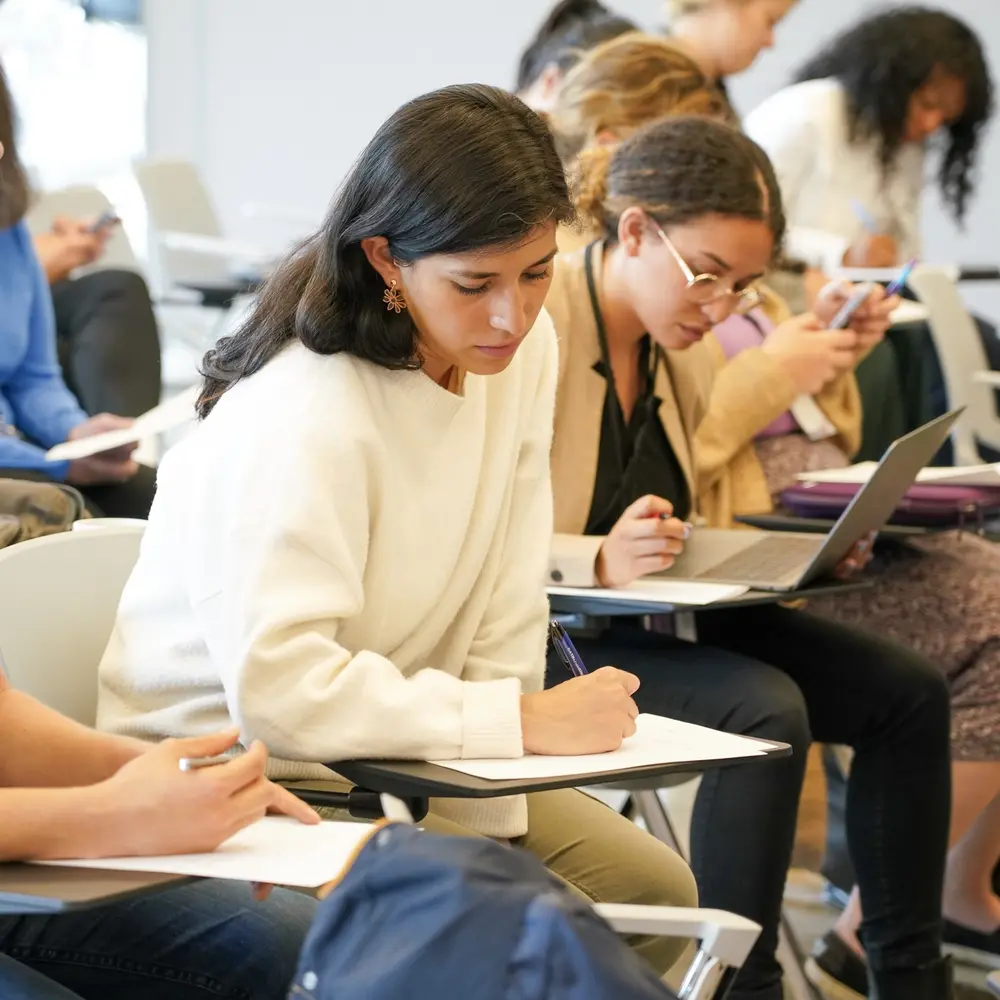A woman writes in her notebook during a presentation. 