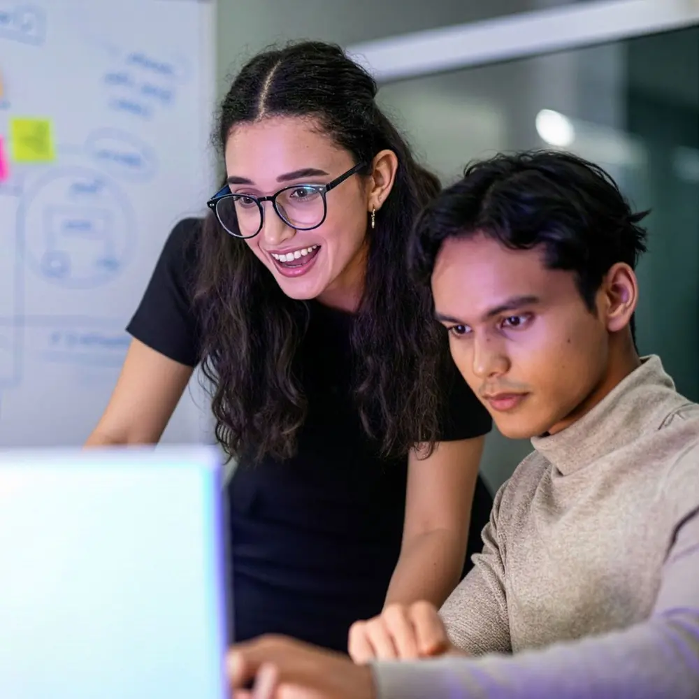 a young women and a young man looking at a computer screen with post it on a whiteboard in the backgorund