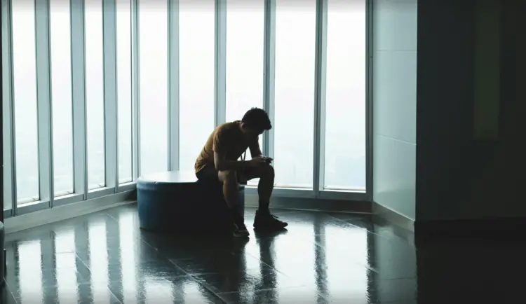 Un jeune homme seul assis sur un banc, regardant son téléphone
