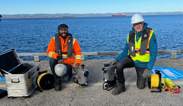 Photo de Jorawar Singh Dham, étudiant à Mila, et Laurent Ferrier posant sur un quai avec leur équipement pour scanner des structures sous-marines.