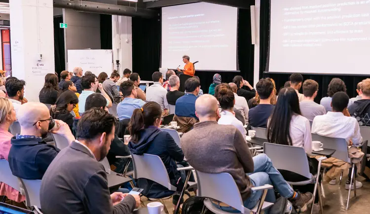 A speaker in front of a full house during Mila's Techaide event