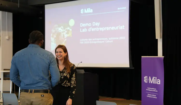 Two participants of Mila's Demo Day talking together in front of the stage