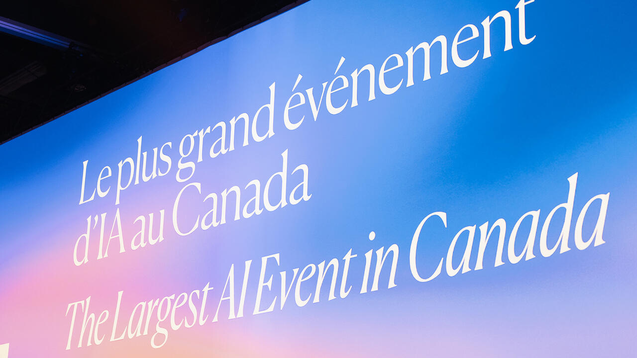 A large screen displaying “ALL IN, the largest AI event in Canada”